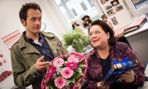 Mit Blumen und Pralinen will Alex (Joris Gratwohl) Frau Kruse (Martina Eitner-Acheampong) vom Gesundheitsamt für sein Start-up „Tischlein-Klick-Dich“ gewinnen.